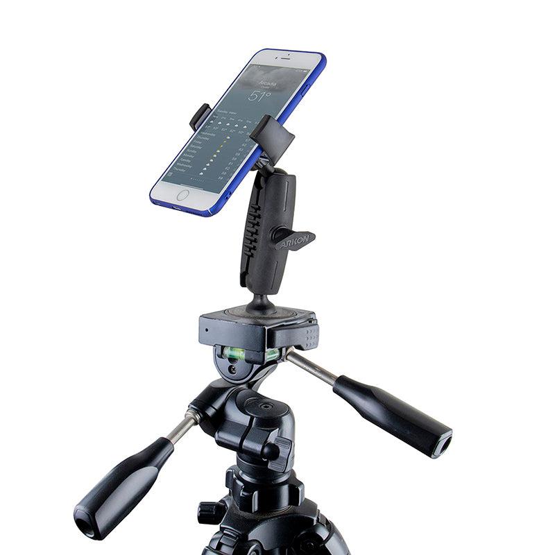 A smartphone mounted on a tripod with the Mobile Grip 5 Tripod Phone Mount displays a weather app. The tripod has two adjustable handles for precise positioning.