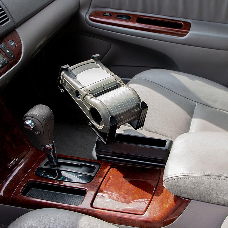 A Mobile Portable Printer Car Truck Seat Wedge Mount for Zebra, Epson, and Brother printers is placed on the armrest between the front seats above the gear shift and cup holders in a car with beige leather seats and wood trim.
