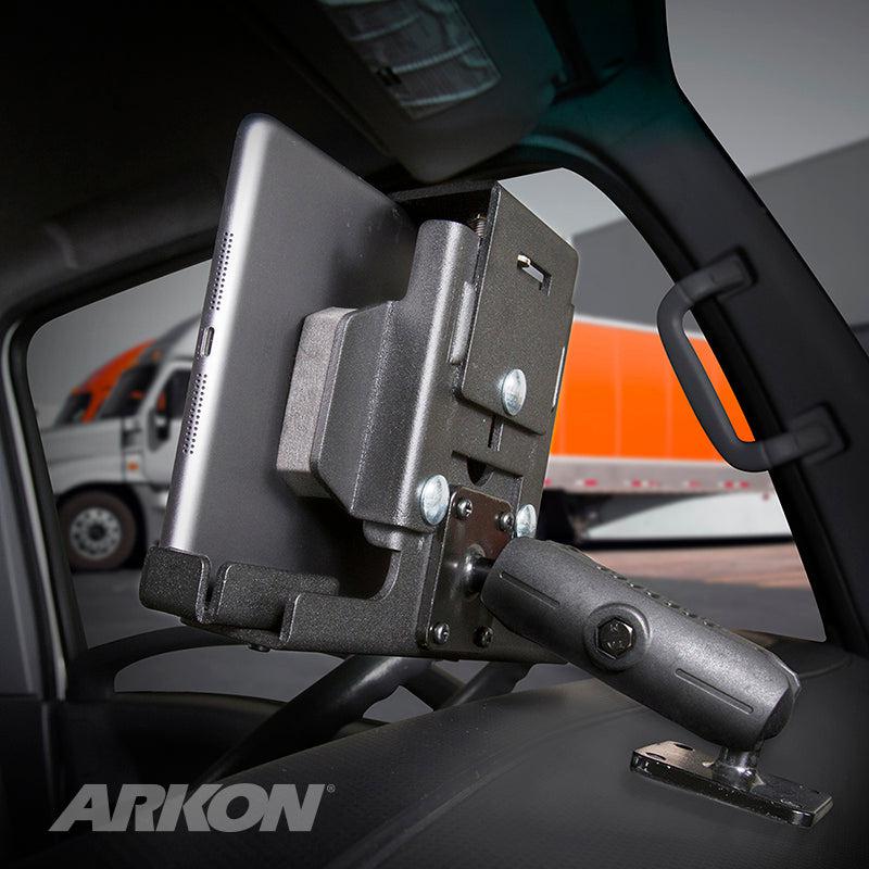 A LockVise™ Metal Locking Tablet Mount with Drill Base and Magnetic USB-C Charge Cable secures a tablet to a vehicle dashboard, with an orange and white truck outside. The word ARKON appears in the lower left corner.