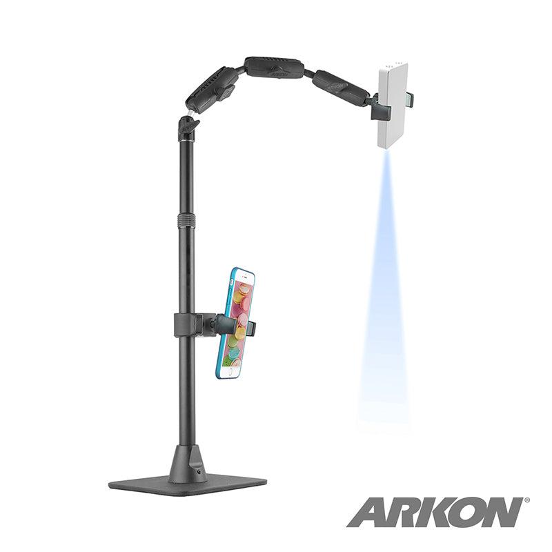The Remarkable Creator™ Cookie Decorators Mount Stand for Phones and Pico Projectors holds a smartphone vertically and a small projector horizontally, projecting light. The ARKON logo appears in the bottom right corner.
