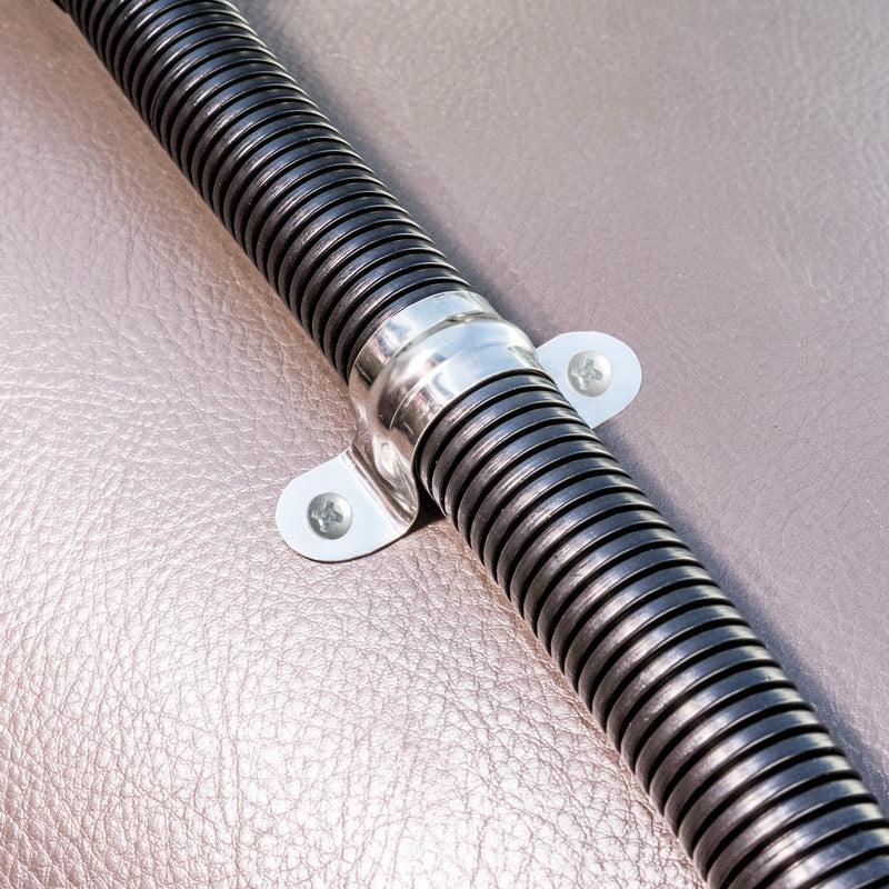 Close-up of a Replacement Metal Conduit for Seat Rail Mounts in black, attached to a textured light brown surface with a shiny metal clamp and two screws for vibration prevention.