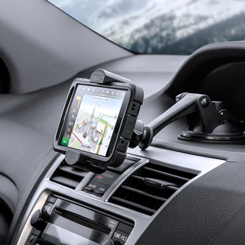 A smartphone is secured on the dashboard with the Sticky Suction Mount and RoadVise® Phone Holder, displaying navigation directions as snowy scenery appears through the windshield in the background.