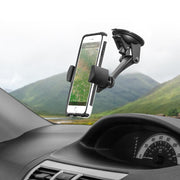 A smartphone secured by the Sticky Suction Mount with RoadVise® Phone Holder displays a map app on the car dashboard, with green hills and a cloudy sky visible outside the window.