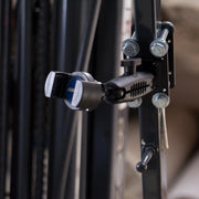 Close-up of the black RoadVise® Forklift Front Guard Phone Mount, featuring bolts, levers, and a blue and white circular element attached to a metal frame, similar to forklift phone holder mechanisms.