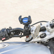 Close-up of a motorcycle handlebar with the RoadVise® Phone Clamp Post Mount for iPhone, Galaxy, Note, and more. Handlebar controls and part of the fuel tank are visible; blurred background emphasizes the mount and handlebar.