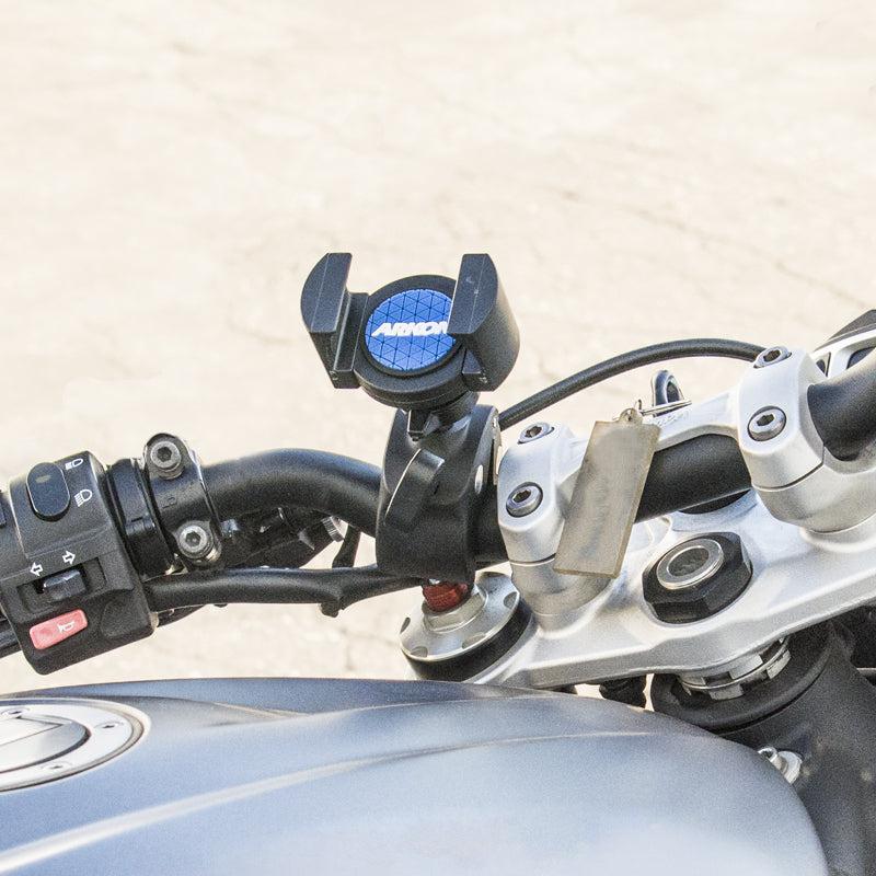 Close-up of a motorcycle handlebar with the RoadVise® Phone Clamp Post Mount for iPhone, Galaxy, Note, and more. Handlebar controls and part of the fuel tank are visible; blurred background emphasizes the mount and handlebar.