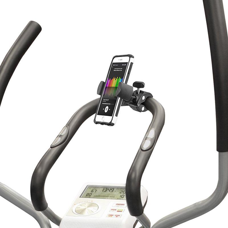 Close-up of an exercise bike handlebar with the RoadVise® Phone Clamp Post Mount holding a smartphone that displays a colorful graph. The bike’s digital screen shows workout stats like time, distance, and calories burned.