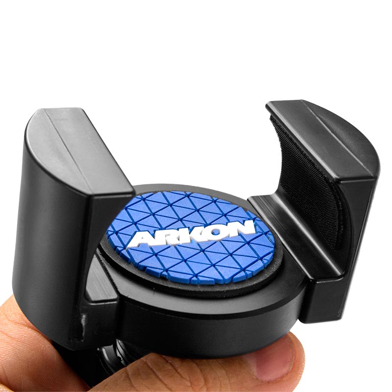 A close-up of a hand holding a RoadVise® Phone Holder with a black frame and a blue circular pad in the center, displaying ARKON in white and compatible with 17mm ball mounts.