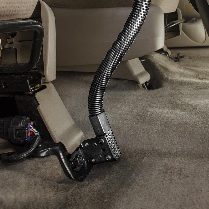 A vacuum cleaner hose cleans the carpet under a car seat, while the RoadVise® Phone Holder with 15 Gooseneck and Seat Rail Mount keeps your device secure and accessible in these hard-to-reach areas.