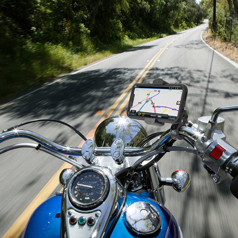 From the rider’s perspective, a motorcycle moves along a tree-lined curve with a RoadVise® Premium Aluminum Motorcycle Handlebar Phone Mount holding a smartphone, its navigation map clearly visible above the dashboard.