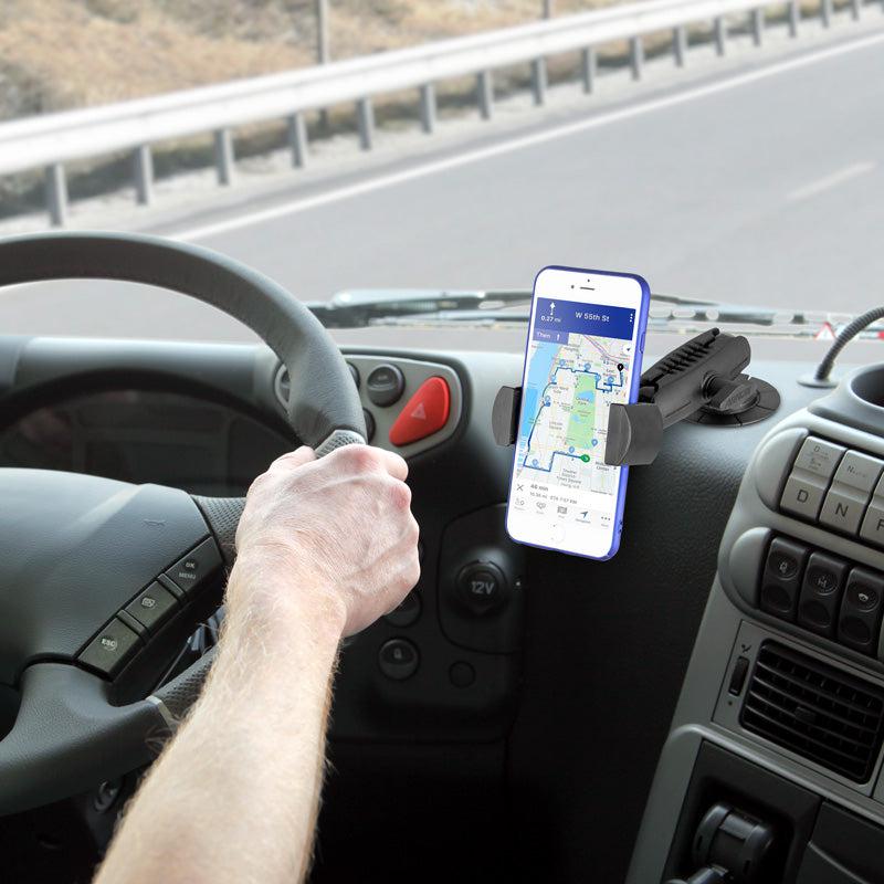 A person drives with their left hand on the wheel, using a GPS navigation app on their smartphone, which is secured by the RoadVise® Phone Holder with Adhesive Car or Truck Mount. The road is visible through the windshield.