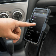 A persons hand touches a smartphone screen on a car dashboard using a RoadVise® XL Car Seat Rail or Floor Mount. The phone shows its settings menu, and car controls appear in the background.