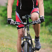 A cyclist in red, black, and white shorts uses the RoadVise® XL Phone and Midsize Tablet Clamp Post Mount to securely hold their smartphone on their mountain bike handlebars while riding on a grassy path.