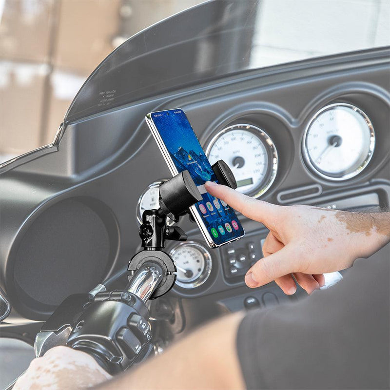 A person uses a smartphone in the RoadVise® XL Premium Aluminum Motorcycle Handlebar Phone and Midsize Tablet Mount, attached to the handlebars with the dashboard and gauges visible in the background.