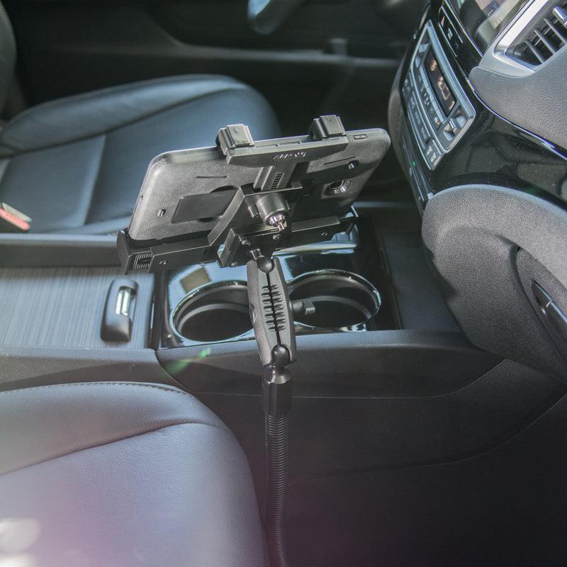 A smartphone is mounted on the LockVise™ Locking Seat Rail Tablet Mount with an 18 aluminum gooseneck, attached to a car’s seat rail between the driver and passenger seats, with the phone facing the driver.