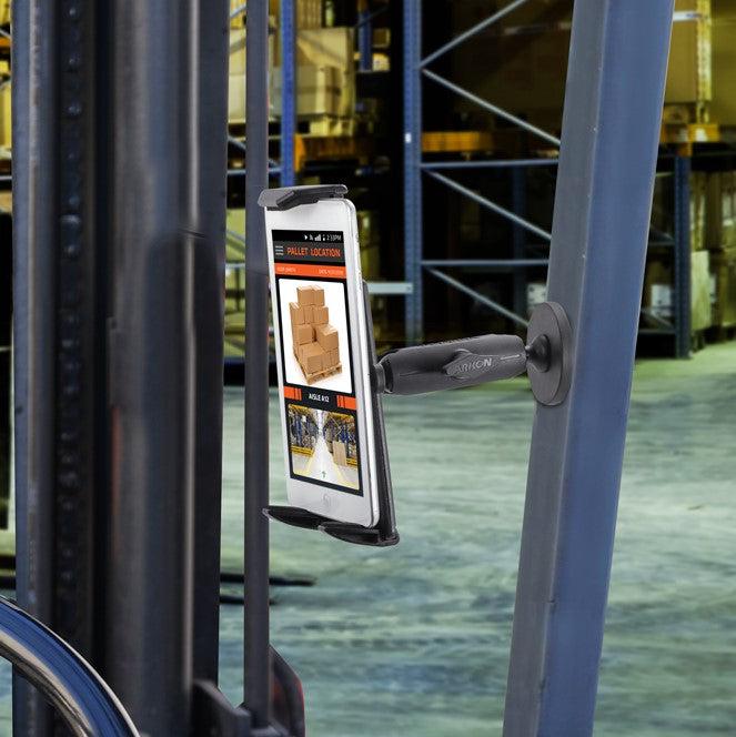 The Robust Magnetic Tablet Mount securely attaches a tablet to a forklift, showing inventory info and box photos, with warehouse shelves full of goods visible in the background.