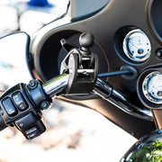 Close-up of a motorcycle handlebar showing mounted controls, rearview mirror, speed gauges, and a Robust™ Mount Clamp Post with 25mm (1) ball attached near the grips for secure device mounting.