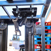 A close-up of the Slim-Grip® Overhead Guard Forklift Tablet Mount with 5 Shaft installed on a forklift, with colorful plastic pallets stacked in the background.