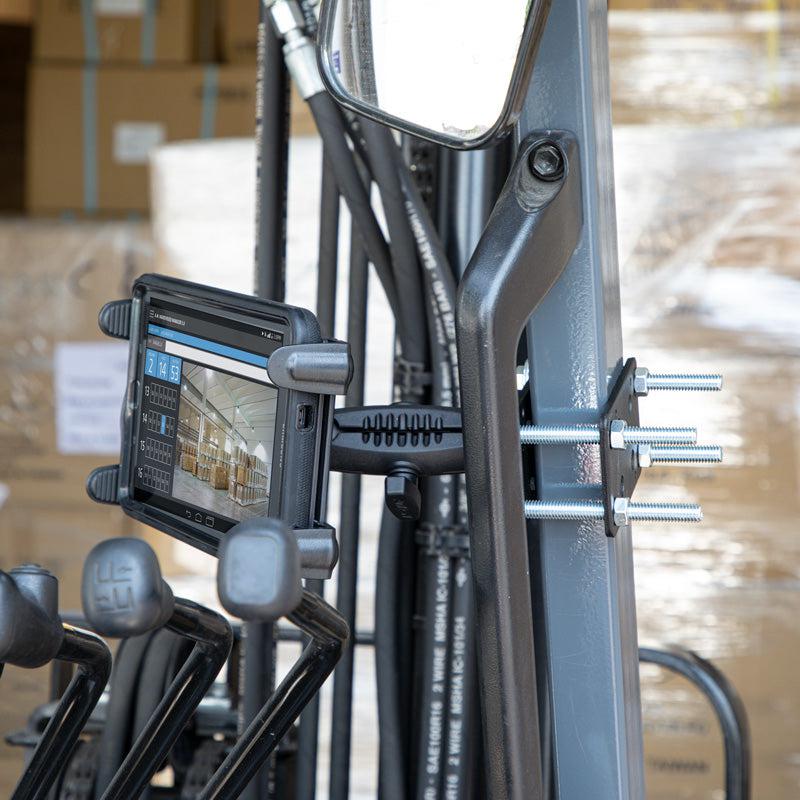 The Slim-Grip® Tablet Holder with Forklift Front Guard Mount and 3.75 Shaft is securely attached to a forklift, displaying a warehouse scene with stacks of cardboard boxes visible in the background.