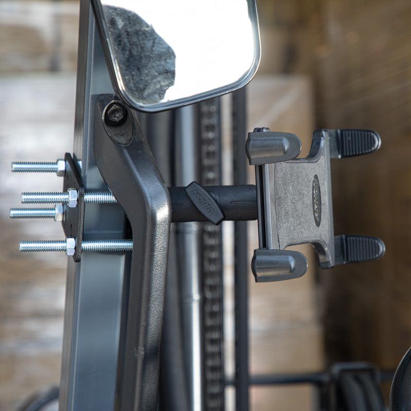 Close-up of the Slim-Grip® Tablet Holder with Forklift Front Guard Mount and 3.75 Shaft securely attached to a metal bar beside a rearview mirror, highlighting its sturdy design ideal for warehouse use.