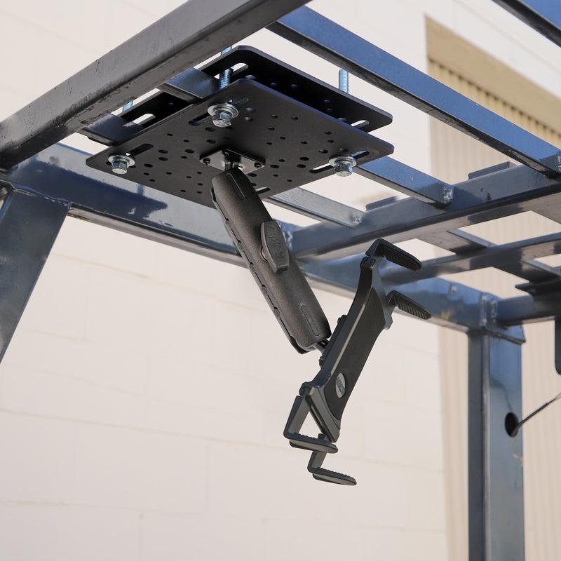 A Slim-Grip® Tablet Holder with Forklift Overhead Guard Mount and 6 Metal Shaft securely installed under a metal frame outdoors by a beige brick wall.