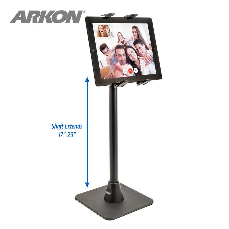 A black Slim-Grip® Tablet Holder with Height-Adjustable Desk Stand secures a tablet on a video call with five people. A blue arrow highlights the adjustable shaft range of 17–29 inches. The ARKON logo is in the top left corner.
