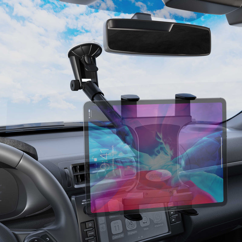 A Slim-Grip® Tablet Holder with Windshield Suction Mount and Extension Arm is attached to a car dashboard. The steering wheel, rearview mirror, and dashboard controls are visible, framed by blue sky and clouds outside.