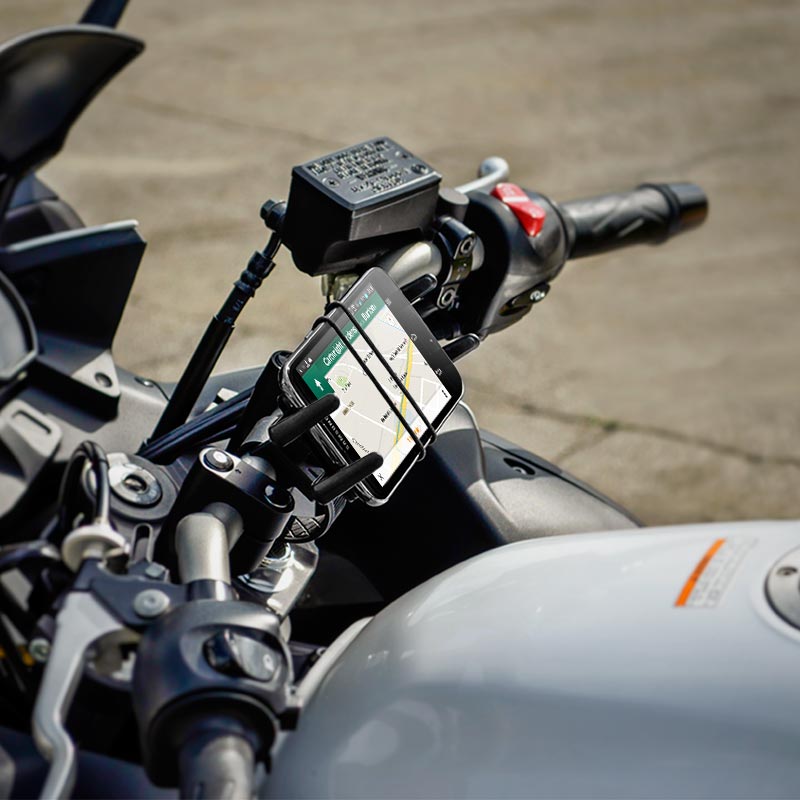 Close-up of a motorcycle handlebar with the Slim-Grip® Ultra Bike or Motorcycle Handlebar Phone Mount holding a smartphone displaying GPS navigation. This secure phone holder keeps your device stable against a blurred concrete background.