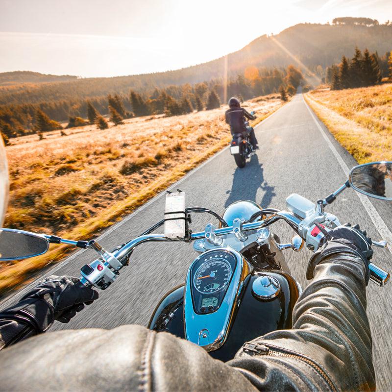 From a motorcyclist’s view riding a scenic road at sunset, the Slim-Grip® Ultra Phone Holder with Motorcycle Handlebar Mount and 2.75 Shaft keeps the GPS steady on the handlebars while warm light spills over hills and fields ahead of another rider.