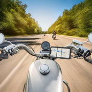 Point-of-view shot from a motorcycle rider on a sunny road, with the Slim-Grip® Ultra Premium Aluminum Motorcycle Handlebar Smartphone Mount visible on the handlebars. Trees line both sides and other motorcyclists are seen ahead in the distance.