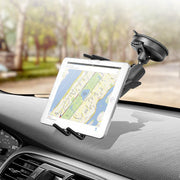 A tablet displays a navigation map on a car dashboard, held securely by the Slim-Grip® Ultra Windshield Mount for iPhone, Galaxy, Note, iPad and more. Trees and a blurred road can be seen through the windshield.