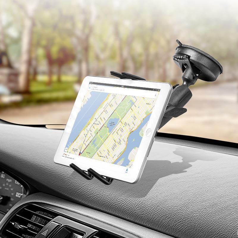 A tablet displays a navigation map on a car dashboard, held securely by the Slim-Grip® Ultra Windshield Mount for iPhone, Galaxy, Note, iPad and more. Trees and a blurred road can be seen through the windshield.
