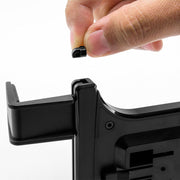 A hand holds a small black plastic piece above a black device, appearing to insert or remove it from a slot—part of the Slim-Grip® Universal Tablet Holder with Dual-T mounting pattern for versatile tablet mounting.