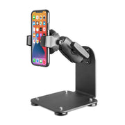 The SteadyMag™ Magnetic Mount System with RoadVise® Ultra Phone Holder is a black adjustable metal stand for warehouse vehicles, securely holding a smartphone upright. Its sturdy base has visible screws, padded feet, and the phone displays app icons.