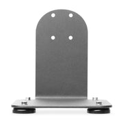 The SteadyMag™ Magnetic Mounting System is a metal L-shaped bracket with four circular holes on the vertical section, mounted on a flat base featuring two round black rubber feet and corner bolts.