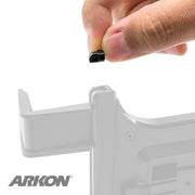 A hand holds a small black Support Stopper for the Slim-Grip® Tablet Holder above an Arkon mount, with the ARKON logo in the lower left. The grayscale image highlights the stopper as the main focus.