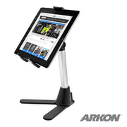 A tablet is shown on a silver and black Desk Stand Mount with Tablet Holder, featuring a sturdy wide base. The tablet displays a website, making the stand ideal for teaching. “ARKON” appears in the lower right corner.