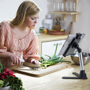 A woman in a peach blouse chops green onions on a wooden cutting board, following a recipe displayed on the Desk Stand Mount with Tablet Holder in her kitchen.