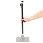A hand holds a vertical black pole above a gray square base from the TW Broadcaster Live Streaming Extension Kit with 29-inch Pole and Dual-T Head, preparing to insert it—ideal for dual phone or live streaming setups.
