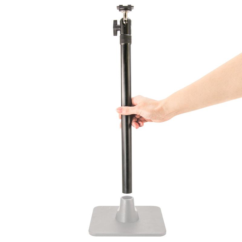 A hand holds a vertical black pole above a gray square base from the TW Broadcaster Live Streaming Extension Kit with 29-inch Pole and Dual-T Head, preparing to insert it—ideal for dual phone or live streaming setups.