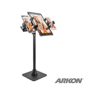 The TW Broadcaster TriStreamer Slim-Grip® by Arkon is a black 29-inch countertop or desk stand that holds two tablets and two phones in adjustable mounts—perfect for live streaming and creators. The Arkon logo appears in the bottom right corner.