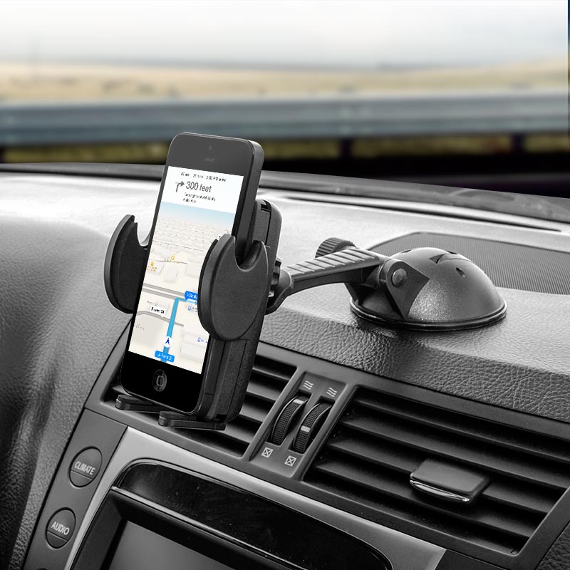 A Windshield or Dash Car Mega Grip™ Phone Holder Mount for iPhone, Galaxy, and Note is attached to the dashboard with a suction cup, holding a phone displaying GPS navigation; nearby, car air vents and controls are visible.