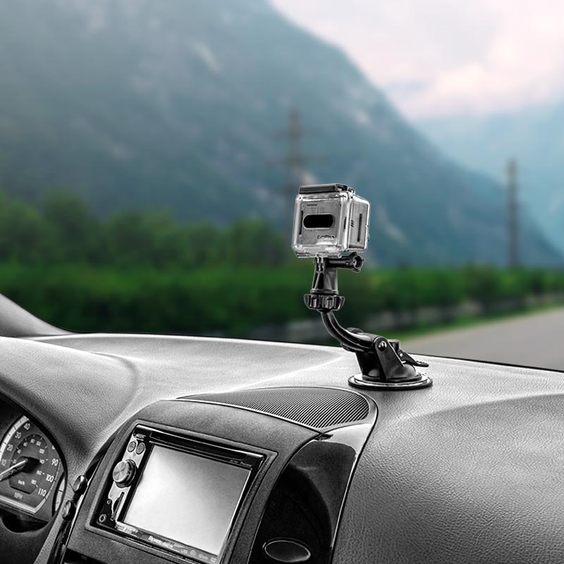 A GoPro HERO Action Camera Holder with Suction Mount and Adhesive Disk is fixed to the dashboard, capturing a blurred view of mountains and greenery through the windshield.
