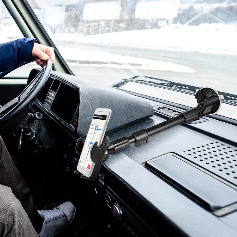A person drives with a Windshield Suction Car Mega Grip™ Phone Mount on the dashboard, holding their smartphone for navigation as snowy scenery appears through the windshield.