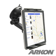 A tablet secured by the Windshield Suction Tablet Mount with Extension Arm in landscape mode displays a map app. The universal holder attaches to the black mount on the car windshield, and the ARKON logo appears in the lower right corner.